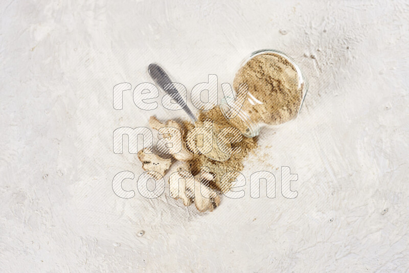 A glass jar full of ground ginger powder flipped with some spilling powder on white background