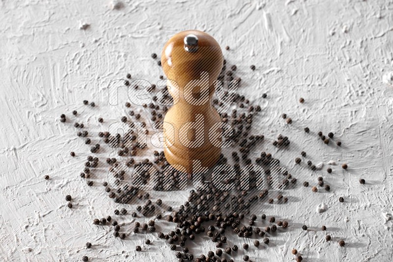 A wooden grinder with black pepper beads on a textured white flooring