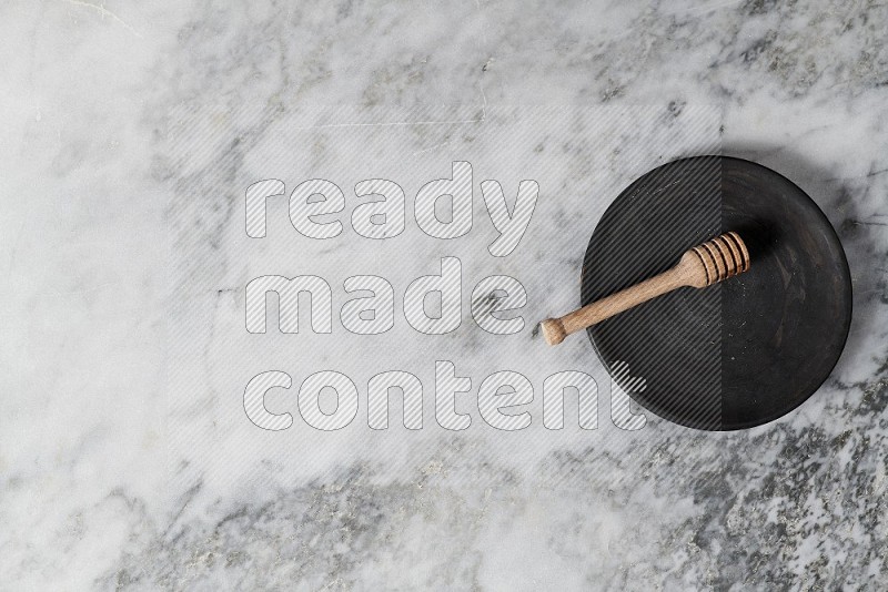 Black Pottery Plate with wooden honey handle in it, on grey marble flooring, Top View