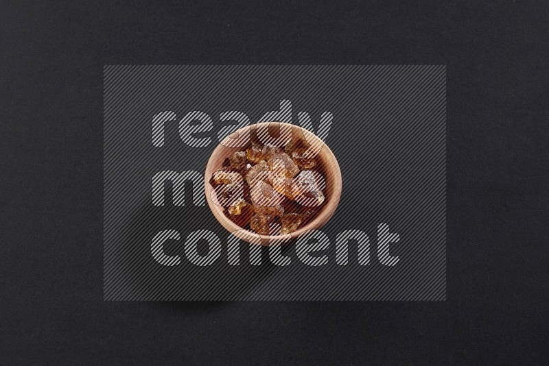 A wooden bowl full of gum arabic on a black flooring in different angles