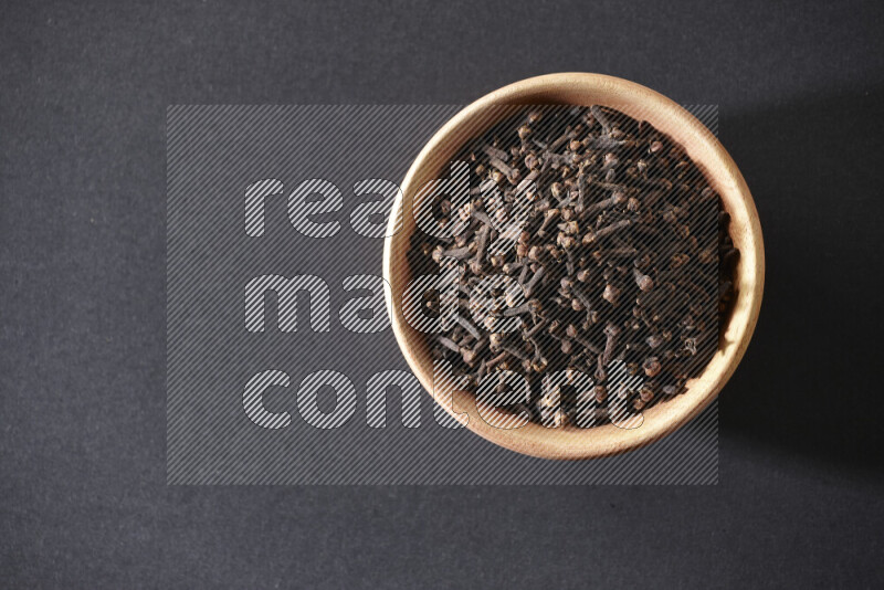 A wooden bowl full of cloves on a black flooring
