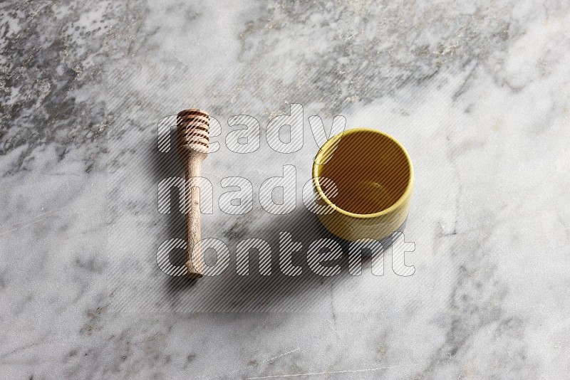 Multicolored Pottery Cup with wooden honey handle on the side with grey marble flooring, 65 degree angle