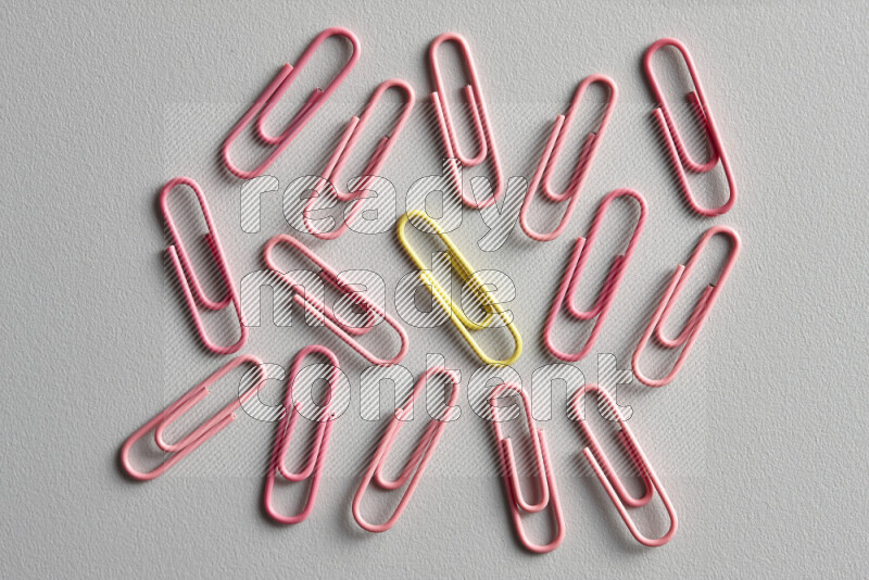 A yellow paperclip surrounded by bunch of pink paperclips on grey background