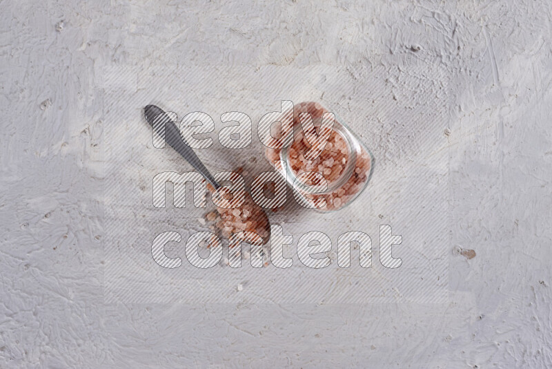 A glass jar full of coarse himalayan salt crystals on white background