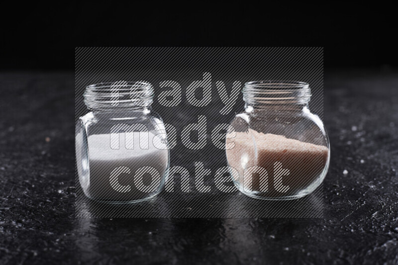 2 glass jars one is filled with fine himalayan salt and the other with table salt on black background