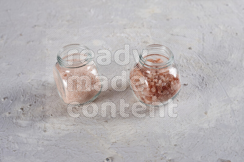 2 glass jars one is filled with fine himalayan salt and the other with coarse himalayan salt on white background