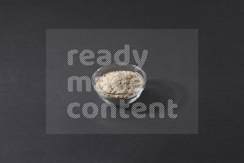 A glass bowl full of garlic powder on a black flooring