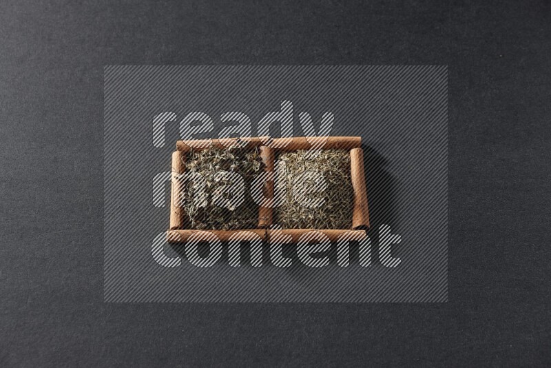 مربعان من أعواد القرفة ممتلئان بحبوب الكمون والريحان المجفف علي خلفية سوداء