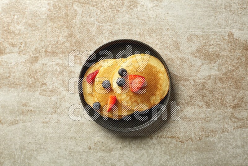 Three stacked mixed berries pancakes in a black plate on beige background