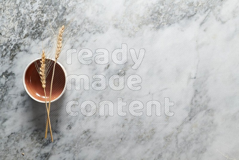 Wheat stalks on Brown Pottery Bowl on grey marble flooring, Top view