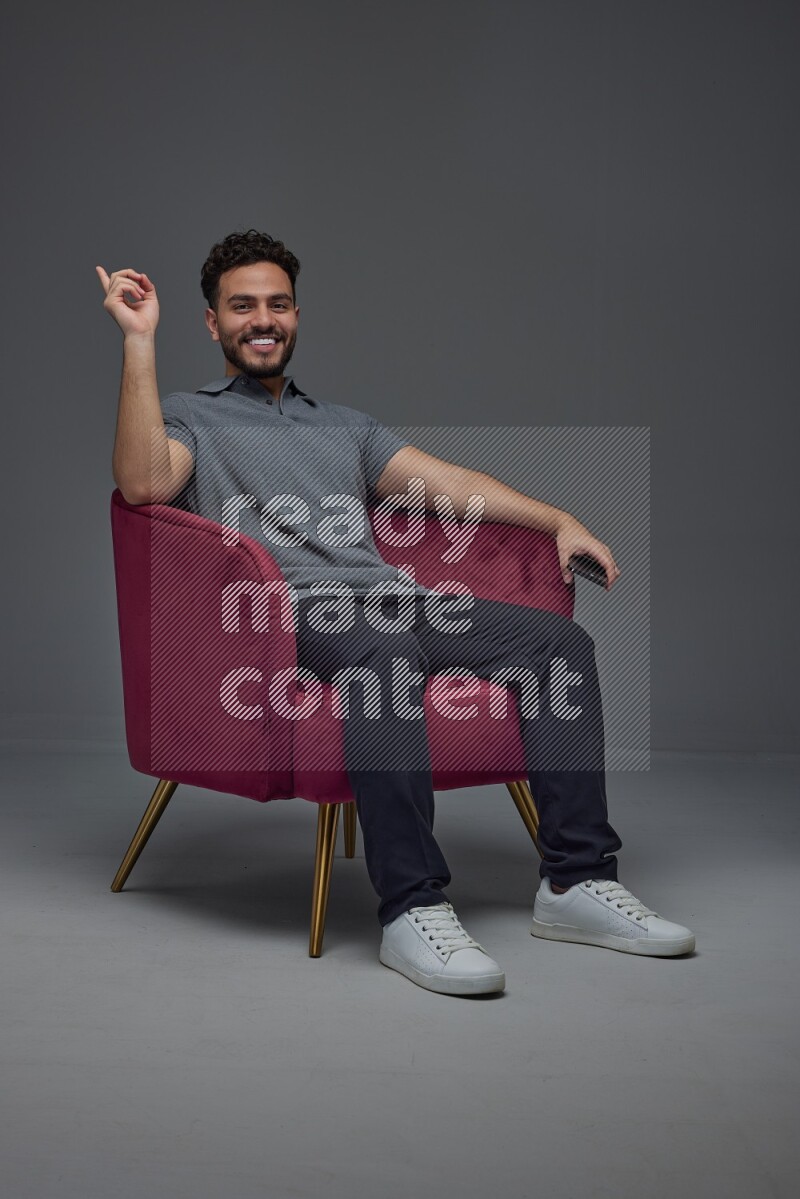 A man wearing casual talking in the phone and making multi hand gestures while sitting on a burgundy chair different angles eye level on a gray background