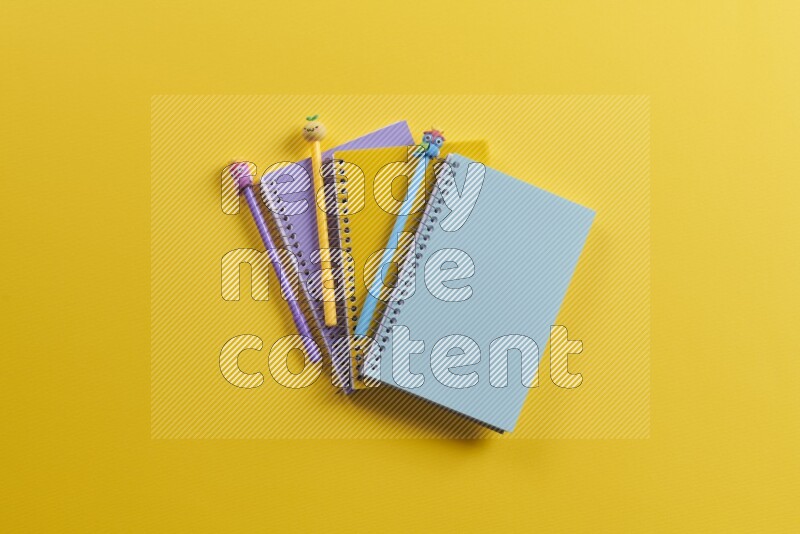 Multicolored notebooks with school supplies on yellow background