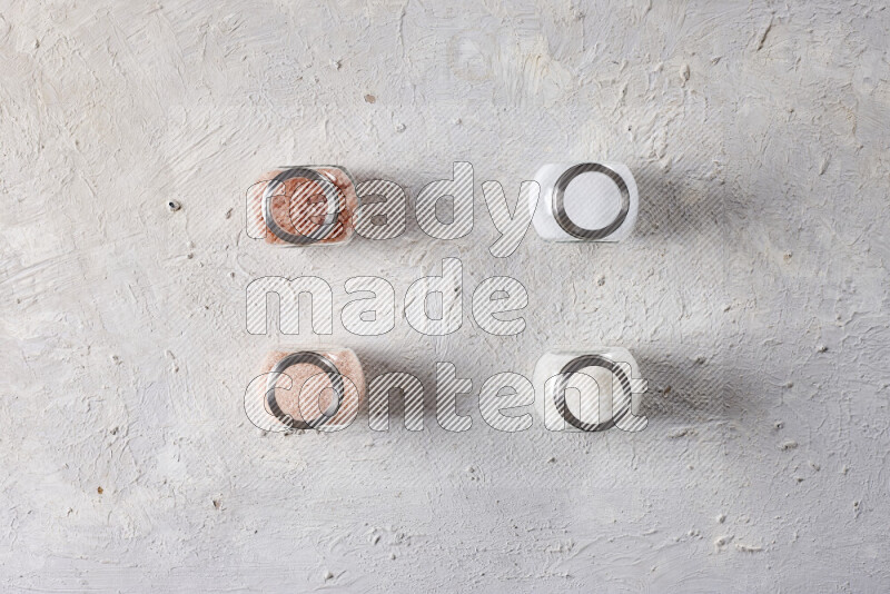 4 glass jars filled with table salt, coarse sea salt, fine himalayan salt and coarse himalayan salt on white background