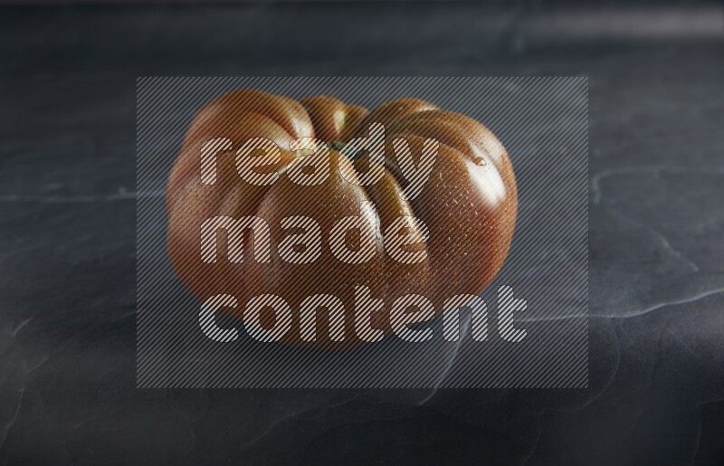 45 degree single heirloom tomato on a textured black slate background