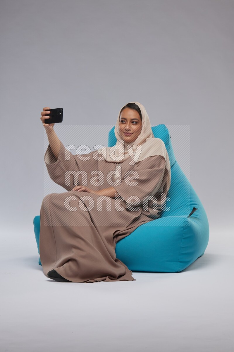 A Saudi woman sitting on a blue beanbag and taking selfie