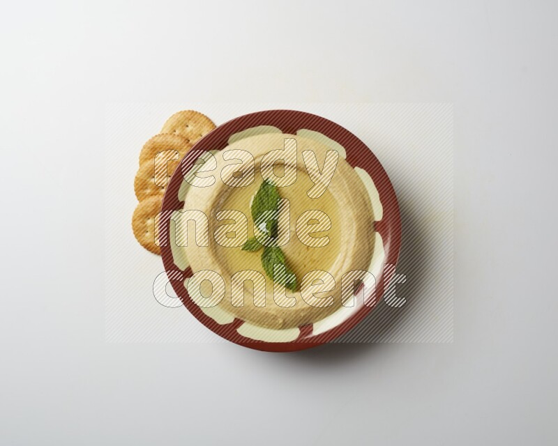 Hummus in a traditional plate garnished with mint on a white background