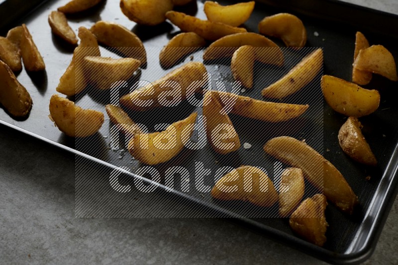 wedges potato in a black stainless steel rectangle tray on grey textured counter top