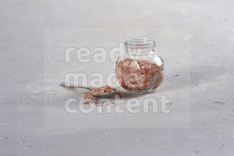 A glass jar full of coarse himalayan salt crystals on white background