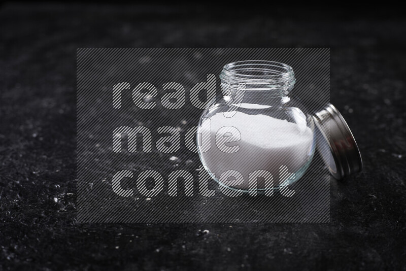 A glass jar full of fine table salt on black background