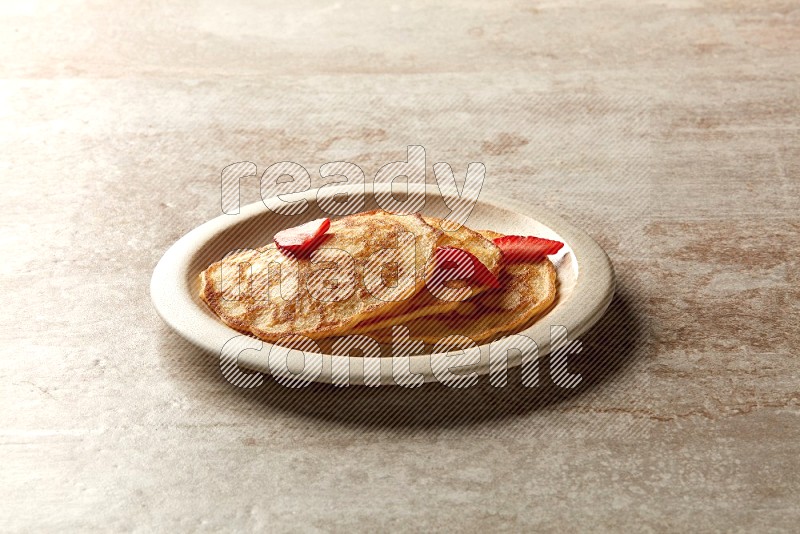 Three stacked strawberry pancakes in a beige plate on beige background