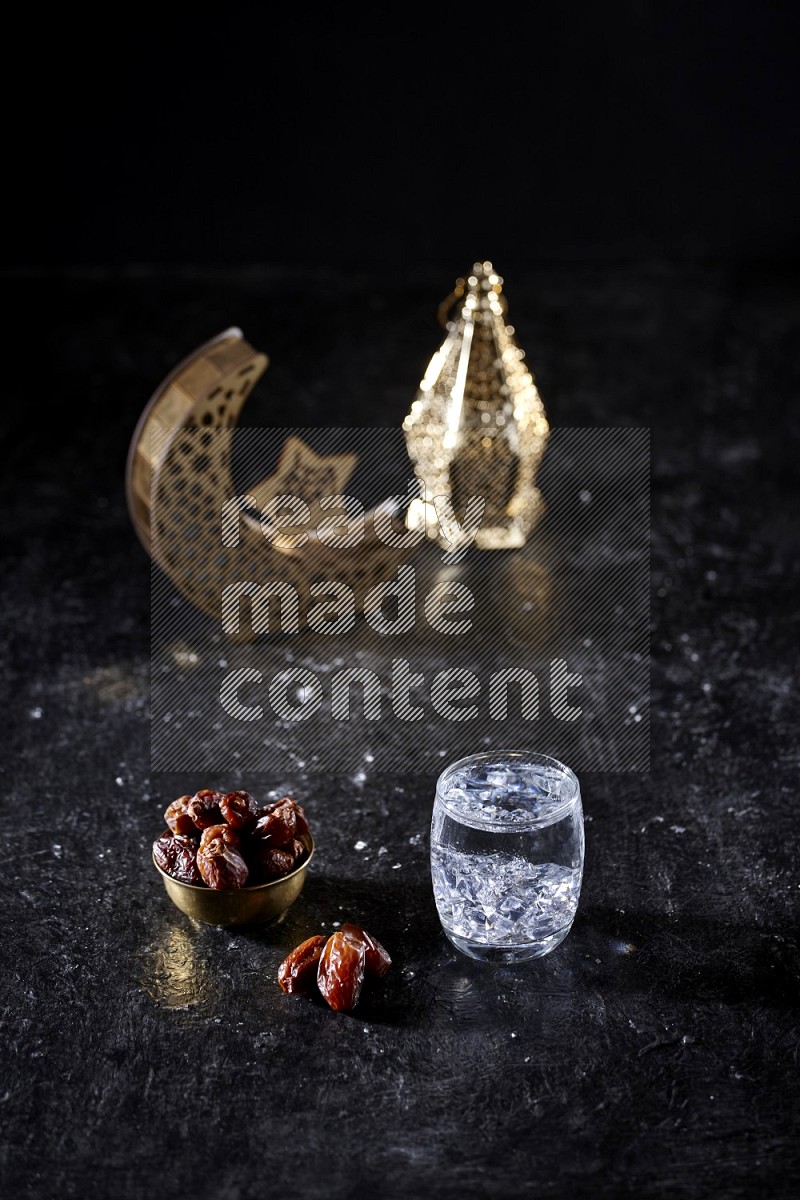 Dates in a metal bowl with water beside golden lanterns in a dark setup