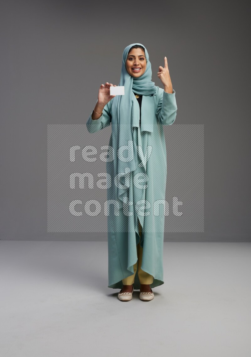 Saudi Woman wearing Abaya standing holding ATM card on Gray background