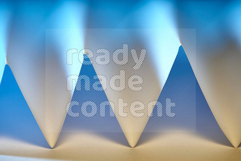 A close-up abstract image showing sharp geometric paper folds in blue gradients and warm tones