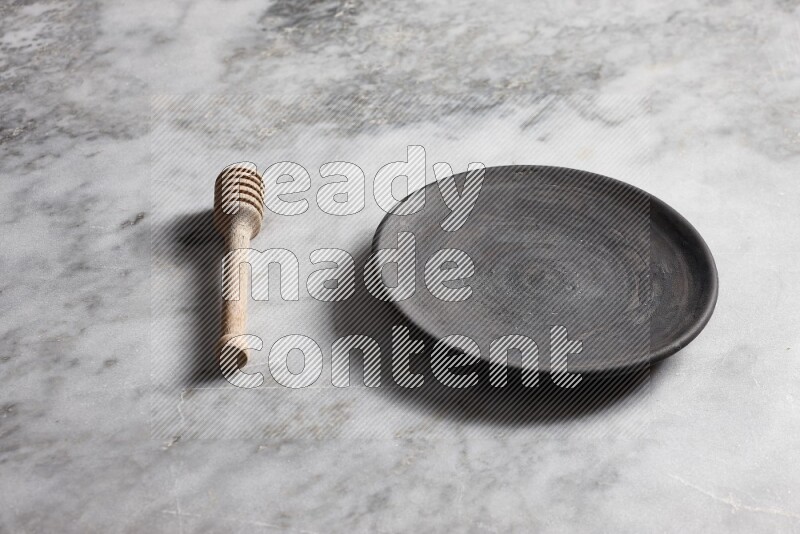 Black pottery plate with wooden honey dipper on the side on grey marble background