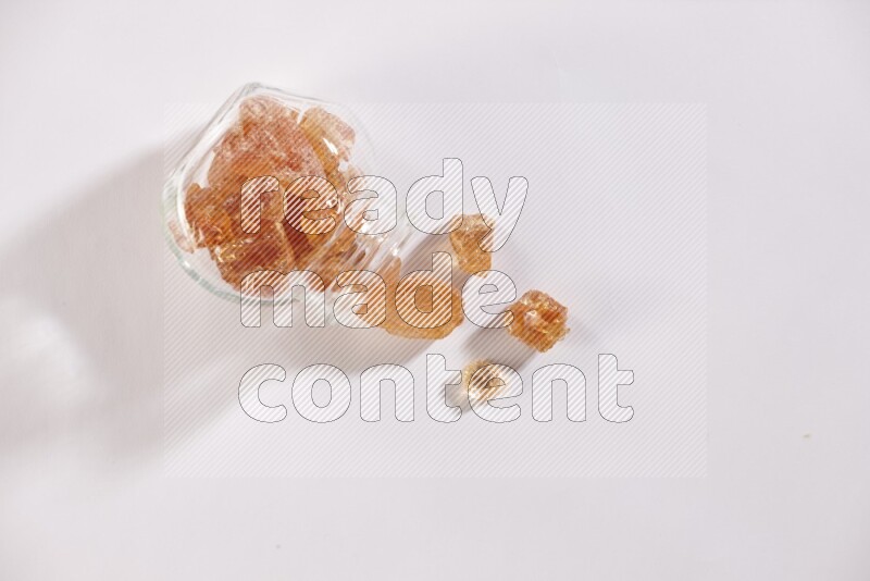 A glass spice jar full of gum arabic and jar is flipped with fallen pieces on white flooring