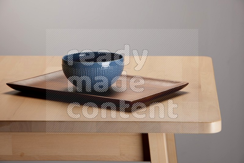 blue bowl placed on a rectangular wooden tray on the edge of wooden table