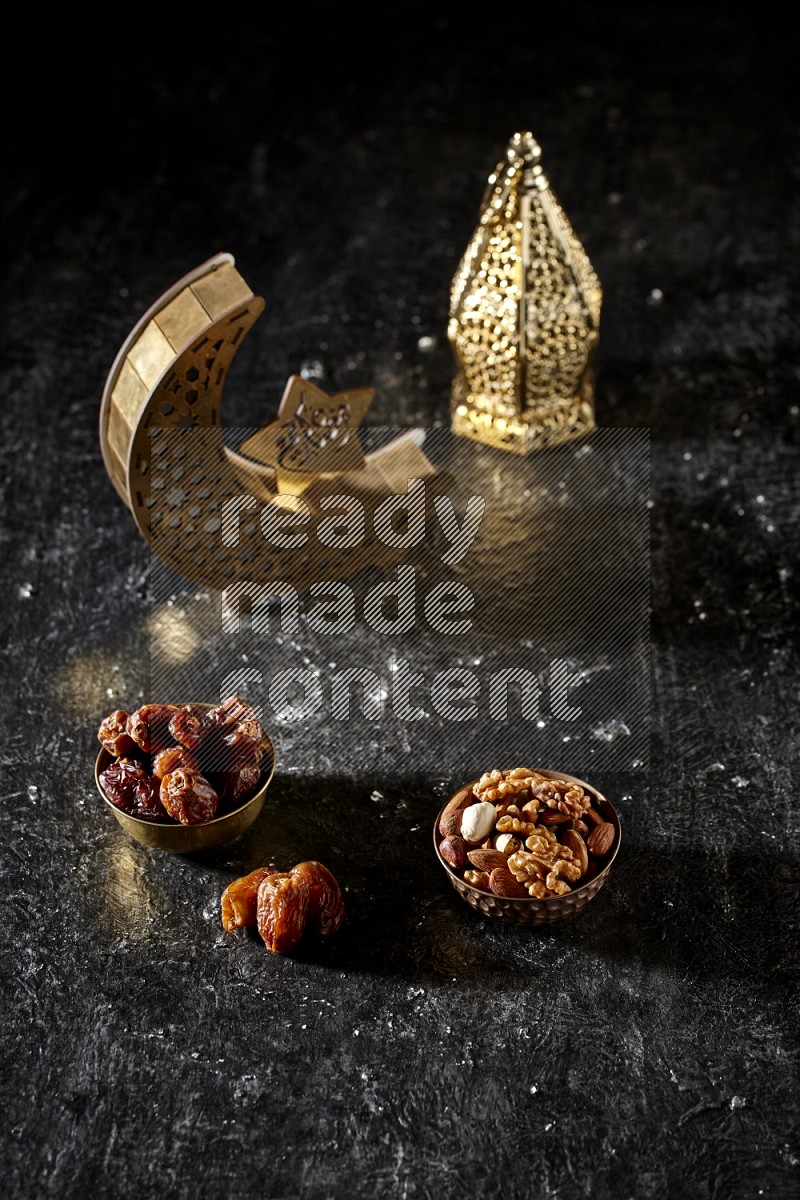 Dates in a metal bowl with mixed nuts beside golden lanterns in a dark setup