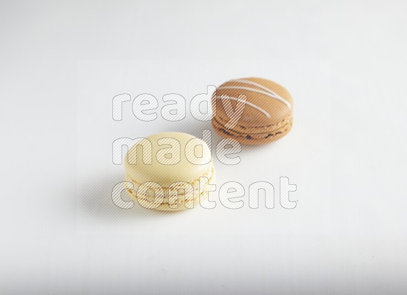 45º Shot of of two assorted Brown Irish Cream, and Yellow Vanilla macarons on white background