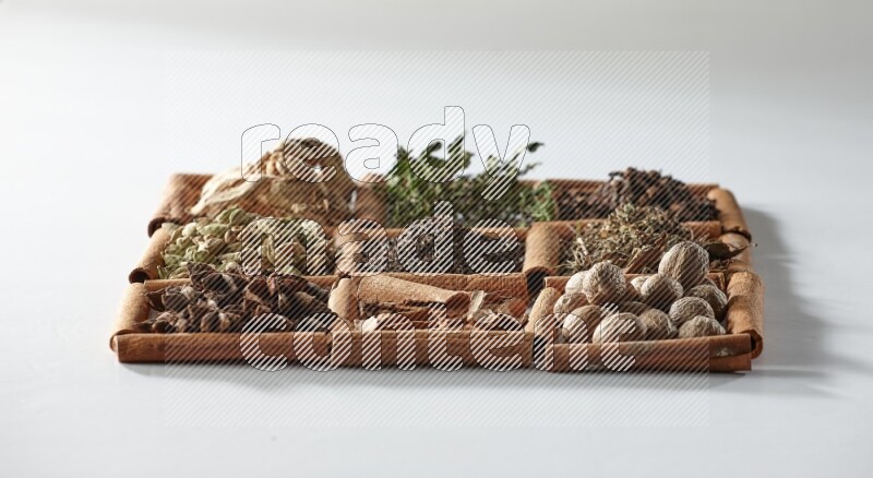 9 مربعات من أعواد القرفة ممتلئة بالشاي في المنتصف محاطة بجوزة الطيب والنعناع المجفف والقرنفل والريحان المجفف والزنجبيل المجفف والقرفة واليانسون والهيل على أرضية بيضاء