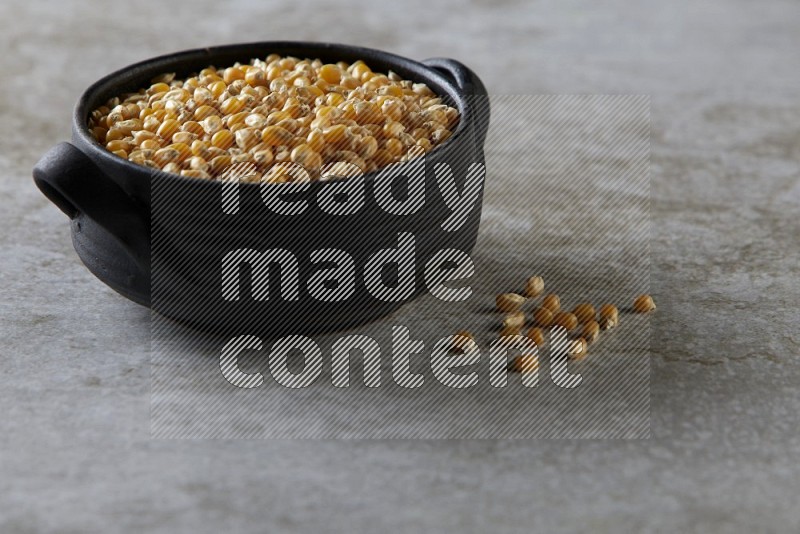 corn kernel in a black handheld ceramic bowl on a grey textured countertop