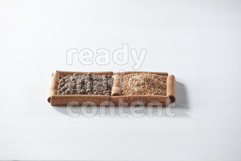 مربعان من أعواد القرفة ممتلئان بحبوب الخردل وحبوب بهار الفلفل الحلو علي خلفية بيضاء