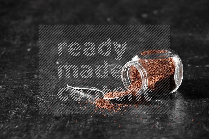 A glass spice jar full of garden cress flipped and seeds spread out and a metal spoon full of the seeds on a textured black flooring in different angles