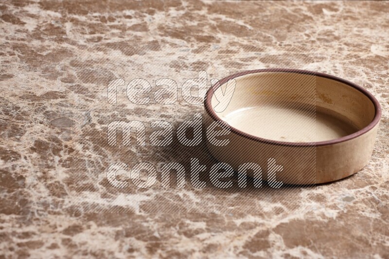 A beige pottery oven plate on beige marble background