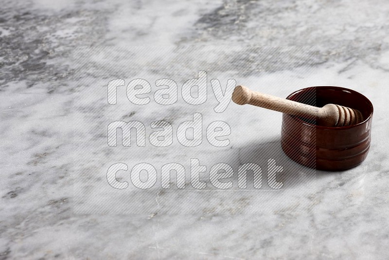 Brown Pottery bowl with wooden honey handle in it, on grey marble flooring, 45 degree angle