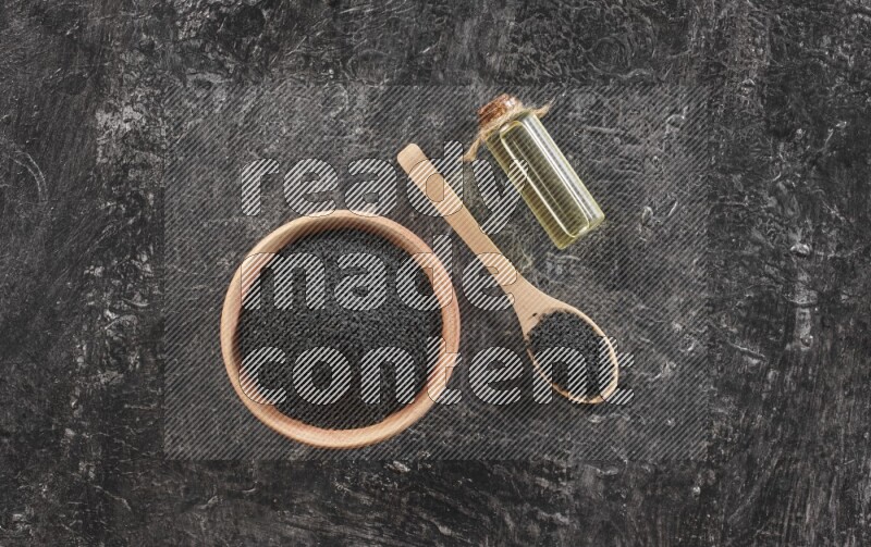 وعاء خشبي وملعقة خشبية ممتلئان ببذور حبة البركة مع زجاجة من زيت حبة البركة علي خلفية سوداء