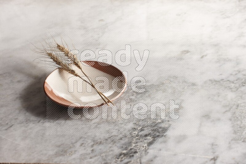 Wheat stalks on multicolored pottery plate on grey marble background