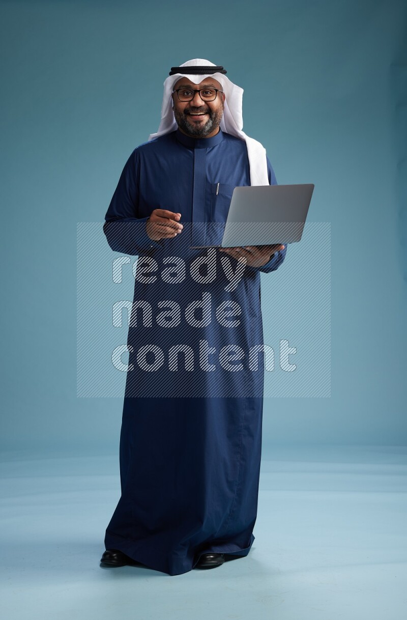 Saudi Man with shimag Standing working on laptop on blue background