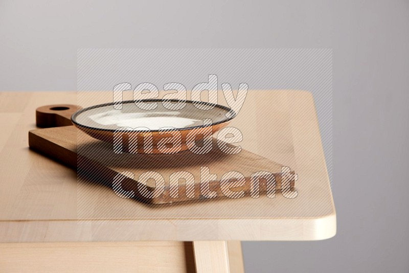 multi-colored pottery Plate placed on a  wooden rectangular cutting board on the edge of wooden table