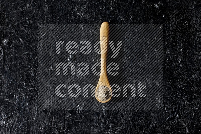 A wooden spoon full of white pepper powder on textured black flooring