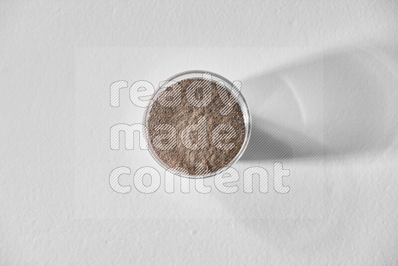 فلفل أسود مطحون في وعاء زجاجي علي خلفية بيضاء