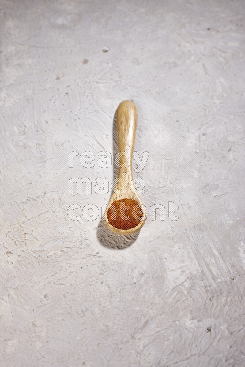 A wooden spoon full of ground paprika powder on white background