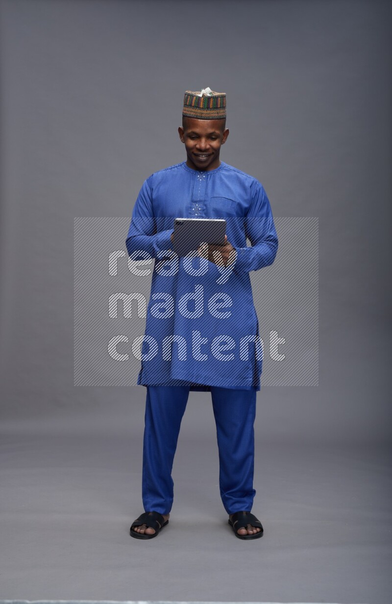 Man wearing Nigerian outfit standing working on tablet on gray background