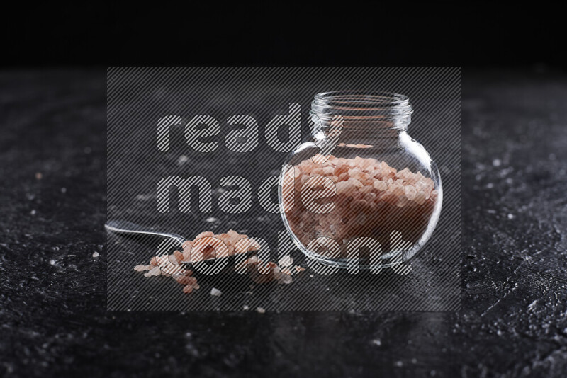 A glass jar full of coarse himalayan salt crystals on black background