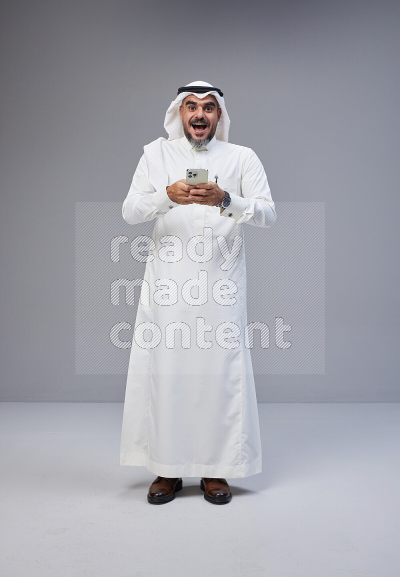رجل سعودي يرتدي ثوب وشماغ ابيض يحمل هاتف جوال