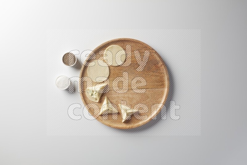 two closed sambosas and one open sambosa filled with cheese while salt, and black pepper aside in a wooden dish on a white background