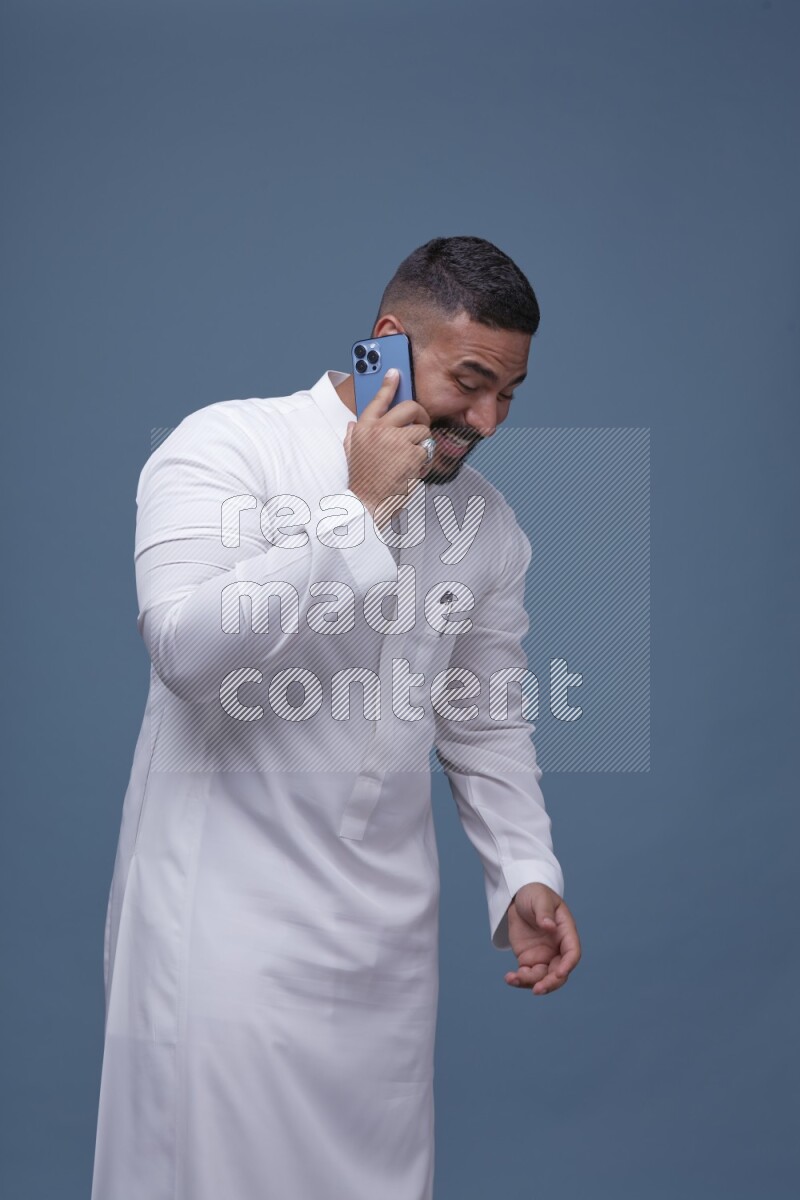 A Saudi man calling on blue background wearing Saudi Thob